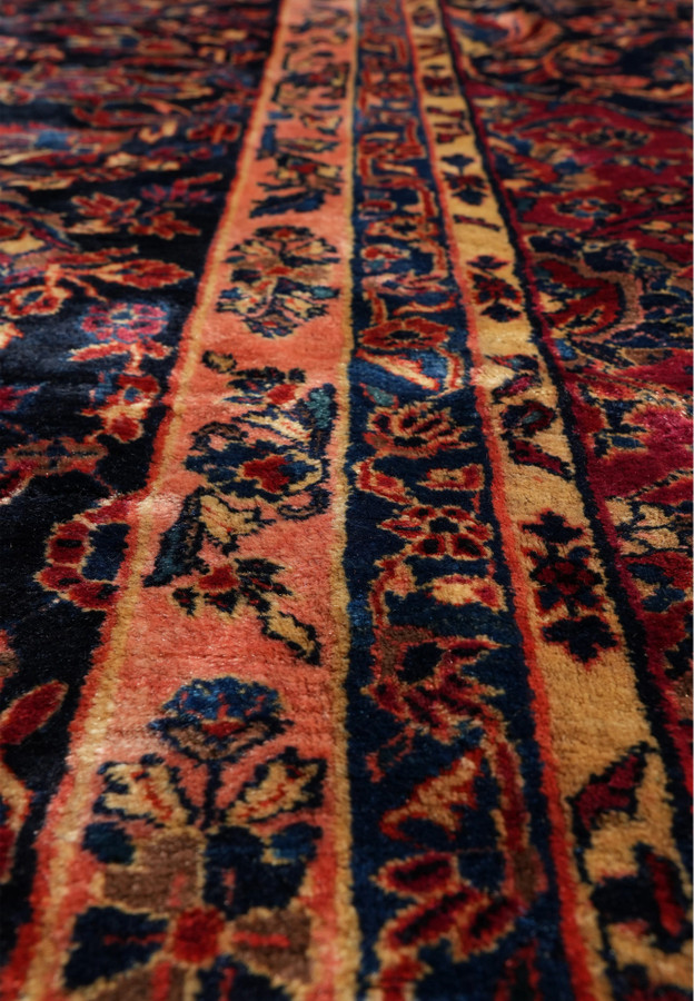 Detailed pattern close-up of antique Kashan rug featuring dense floral motifs in navy, red, and gold with fine knotting and soft aged wool.