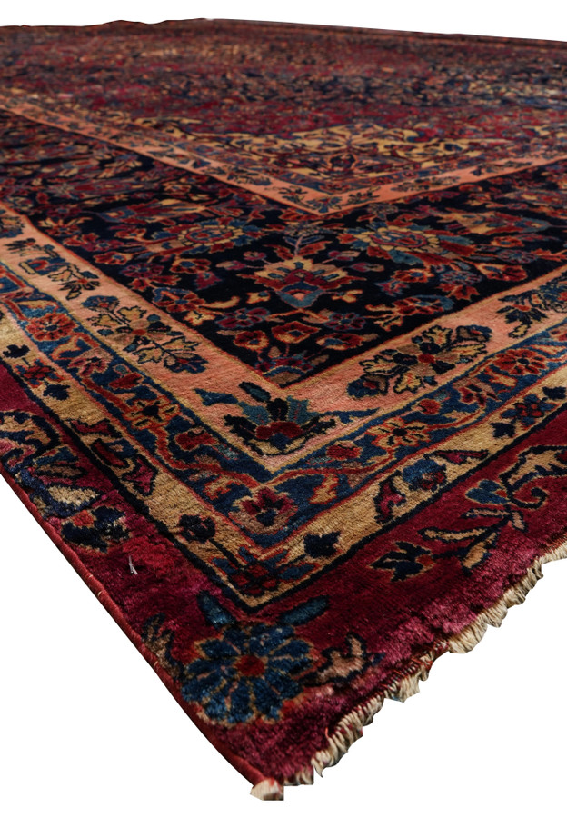 Corner section of Persian Kashan rug showing navy floral border, rose-red field, and golden accent tones in 1930s hand-knotted design.