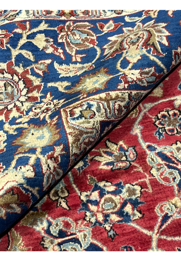 Rolled section of a vintage Najafabad Persian rug showcasing dense floral patterns in red, blue and ivory tones.
