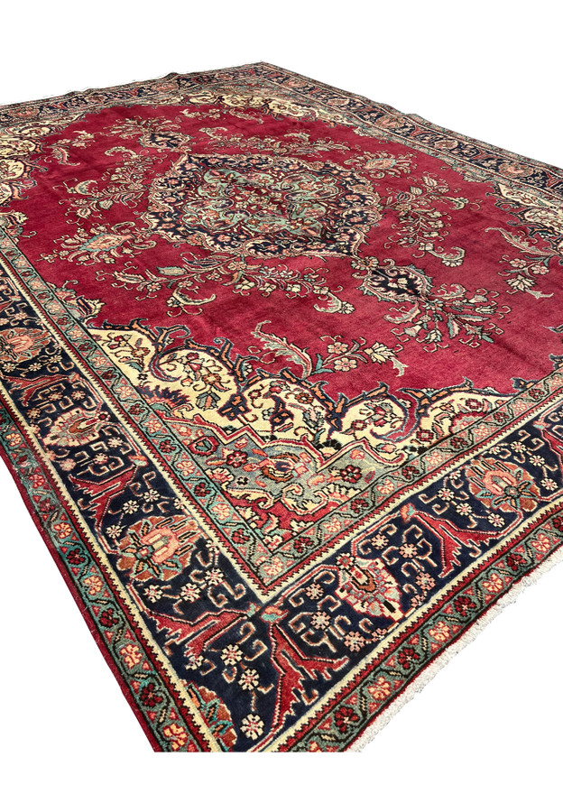 Angled view of the Vintage Persian Tabriz Rug highlighting patina wear, red field, and cream corner spandrels.