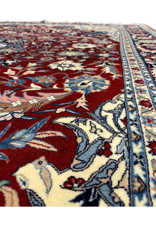Close up of floral pattern on Persian Isfahan rug with dense vines, palmettes, and soft ivory and blue highlights on red field