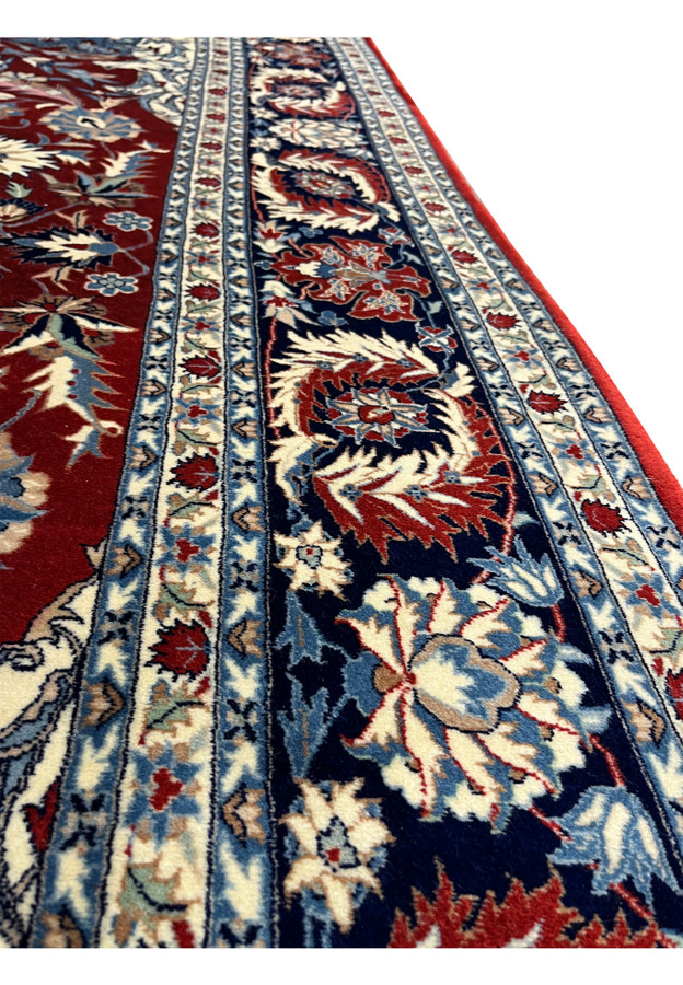 Close-up of Persian Isfahan rug border showing navy floral vines, ivory guard borders, and red field with crisp hand-knotted wool detail.