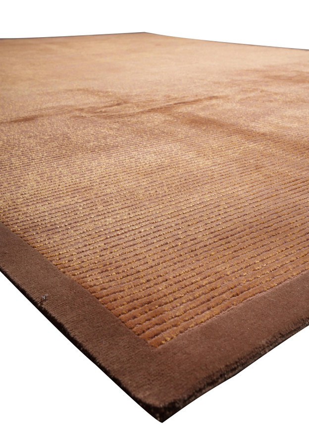 Angled view emphasizing the low pile texture and shimmering silk fibers of this modern Tibetan rug with warm copper and cinnamon tones