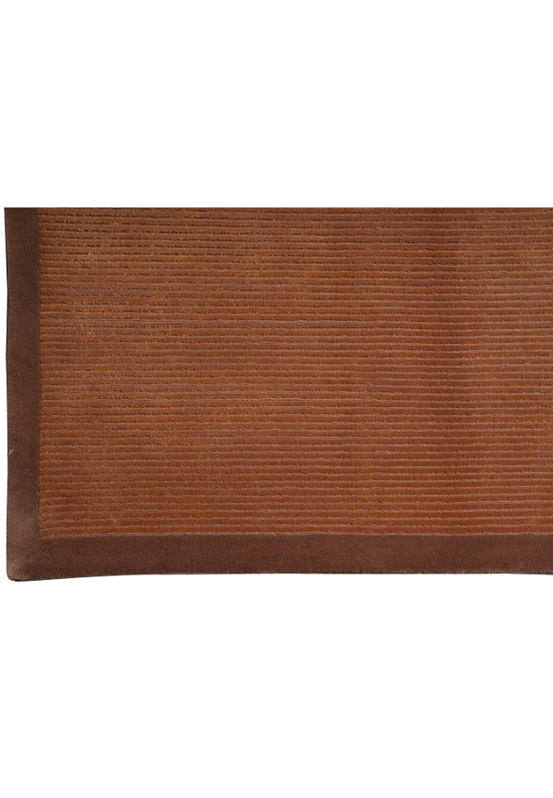 Close-up of the refined border framing this handmade Tibetan rug, showing deeper brown tones that subtly contrast the textured field