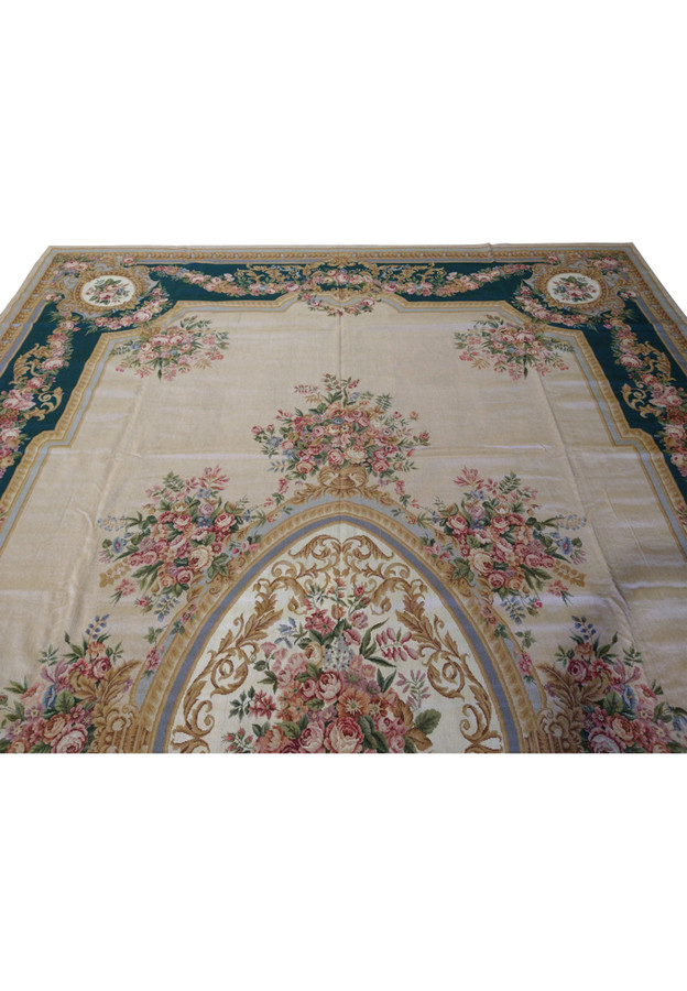 Upper section detail of French Aubusson rug highlighting emerald green border, pink rose garlands, muted gold scrollwork, and beige background