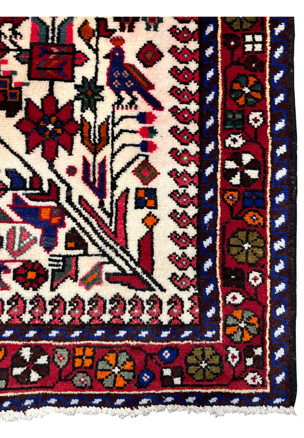 Close-up of Persian Rudbar rug border showing repeating geometric medallions, deep red tones, dark navy accents, and village weaving character.