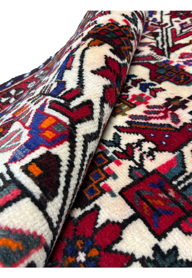 Rolled corner of Persian Rudbar rug revealing thick wool pile, flexible structure, and vibrant village colors across the allover pattern.