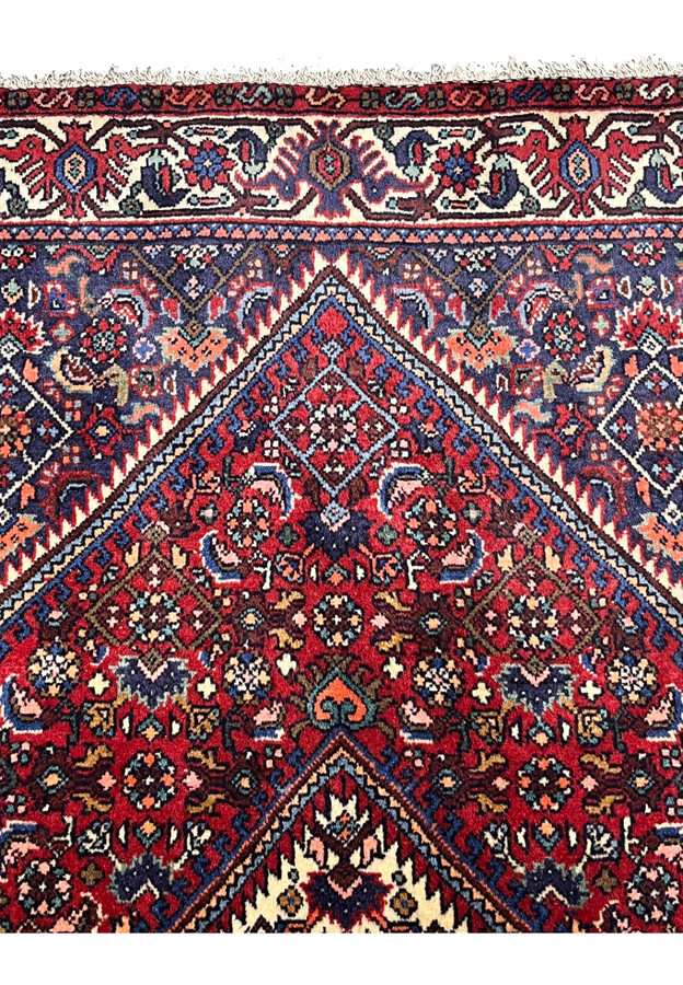 Upper border close-up on a Persian Gholtogh rug with repeating tribal motifs, stylized forms, and strong contrast against the red field.