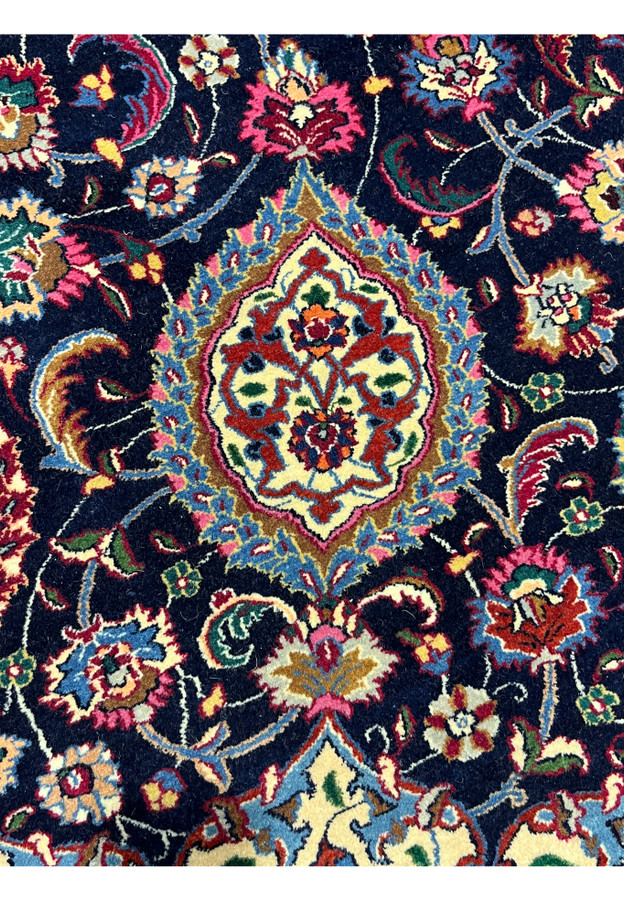 Detailed Persian Mashad rug motif featuring floral medallion elements, intricate curvilinear vines, and silk highlights on a deep navy background