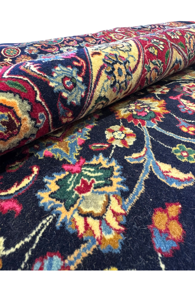 Rolled view of a hand-knotted Persian Mashad rug showing thick pile height, flexible structure, and luxurious kork wool with silk detailing.