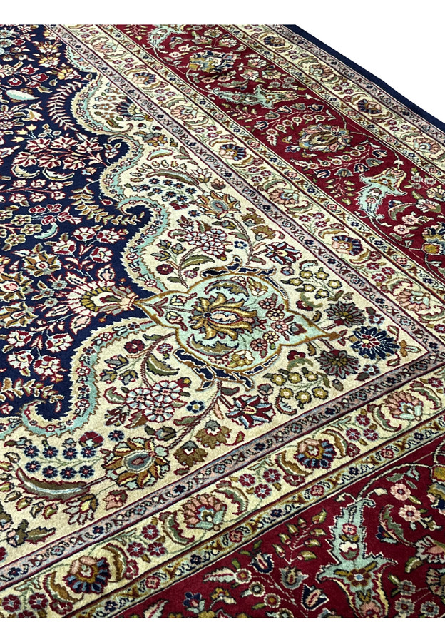 Floral pattern detail on a Persian Tabriz rug showing dense vine work over a deep navy field with ivory and pastel highlights