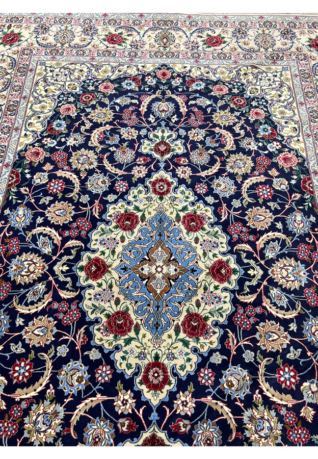 Top view of a 7x10 super fine Persian Isfahan rug with deep navy field, ivory medallion, red floral motifs, and detailed silk highlights
