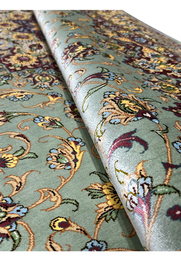 Rolled Persian Qum pure silk rug revealing fine silk pile sheen, dusty sage green field, and intricate floral pattern with burgundy and gold accents
