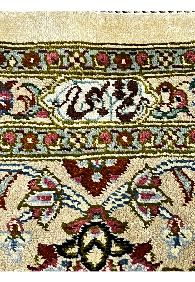 Woven signature cartouche on a Persian Qum pure silk rug framed by floral motifs, confirming workshop origin and fine hand-knotted silk detail.