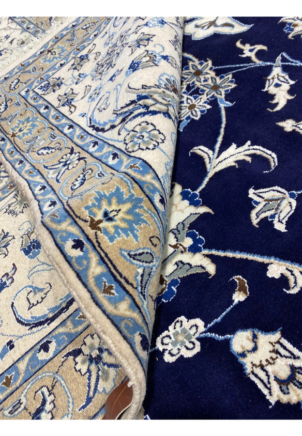 Rolled view of a 10x19 Persian Nain 9 La rug showing fine wool pile, deep navy blue field, ivory floral motifs, and crisp border detailing