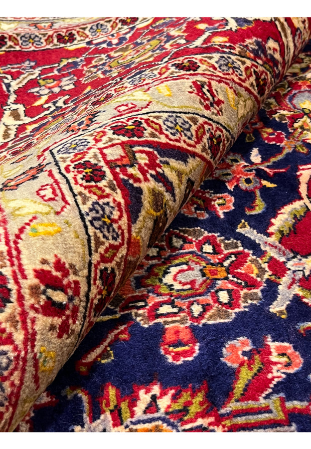 Rolled Persian Isfahan rug emphasizing dense pile, flexible structure, rich navy and red colors, and fine traditional craftsmanship