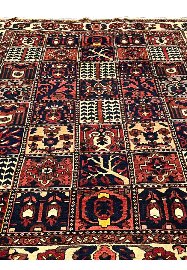 Midfield detail of a Persian Bakhtiar garden pattern rug highlighting pictorial square panels with tree motifs, floral symbols, navy blue grounds, and red accents