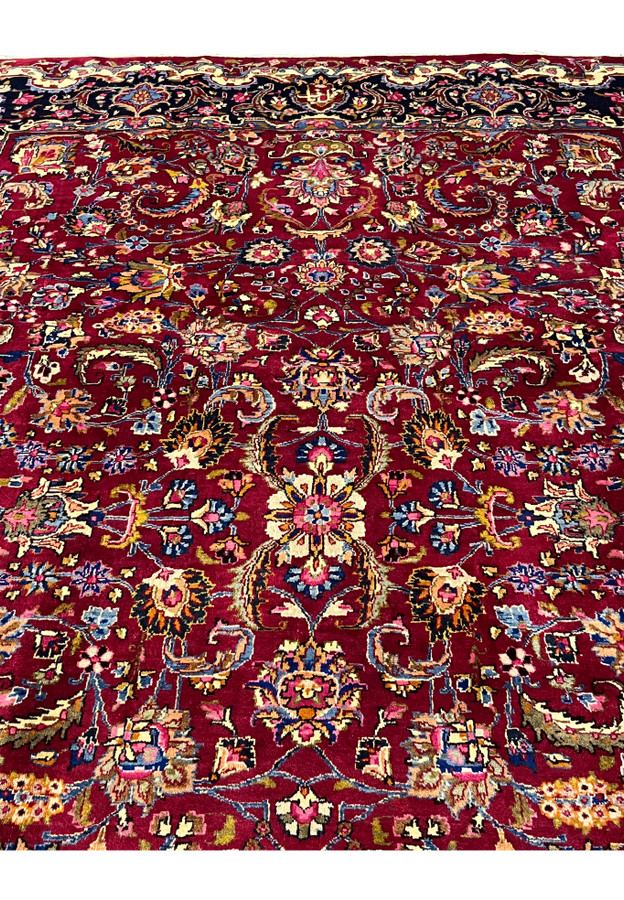 Close view of Mashad rug field showing dense floral arabesques, vibrant red background, and fine wool knotting