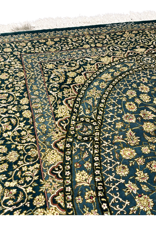 Close view of Persian Qum silk rug showing dense floral vines and arabesque motifs on teal blue field with ivory blossoms and fine 1000 KPSI knot detail