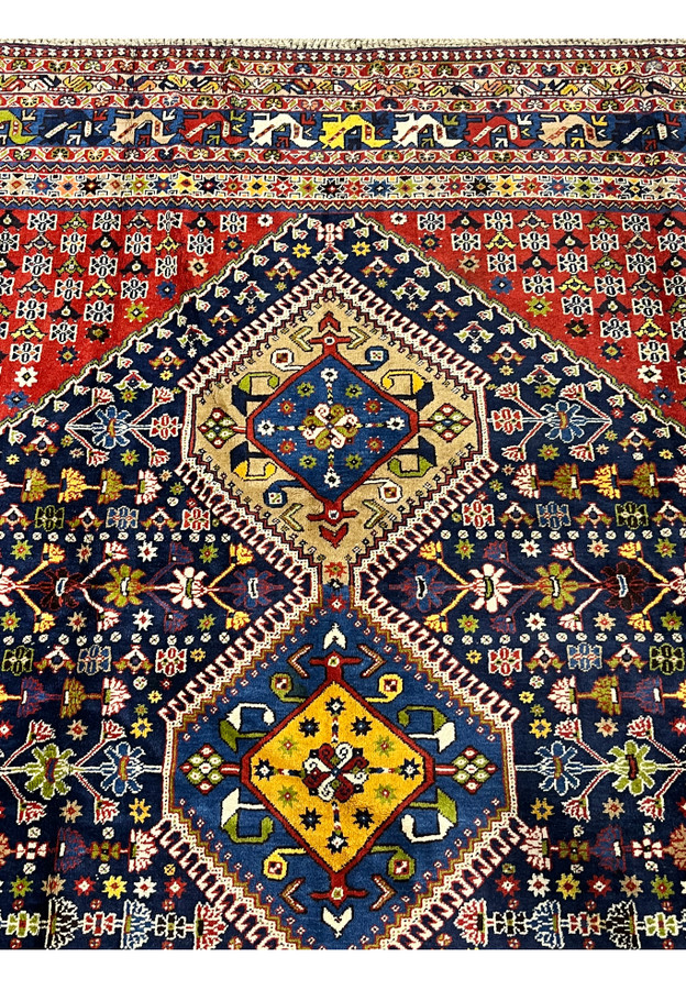 Yalameh tribal rug upper field close up in deep red with repeating geometric flower motifs and navy corner spandrel