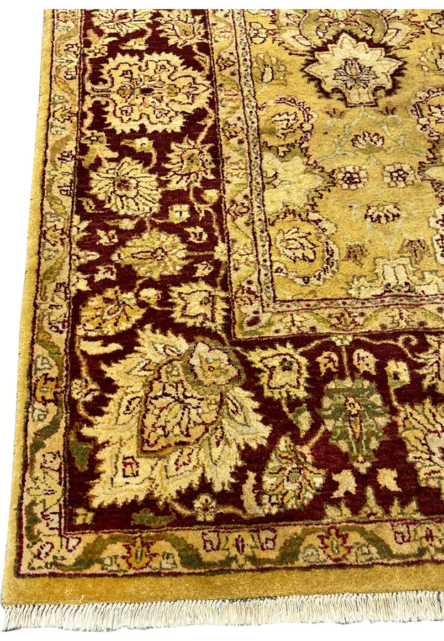 Close view of burgundy main border with large floral motifs on gold Agra rug.