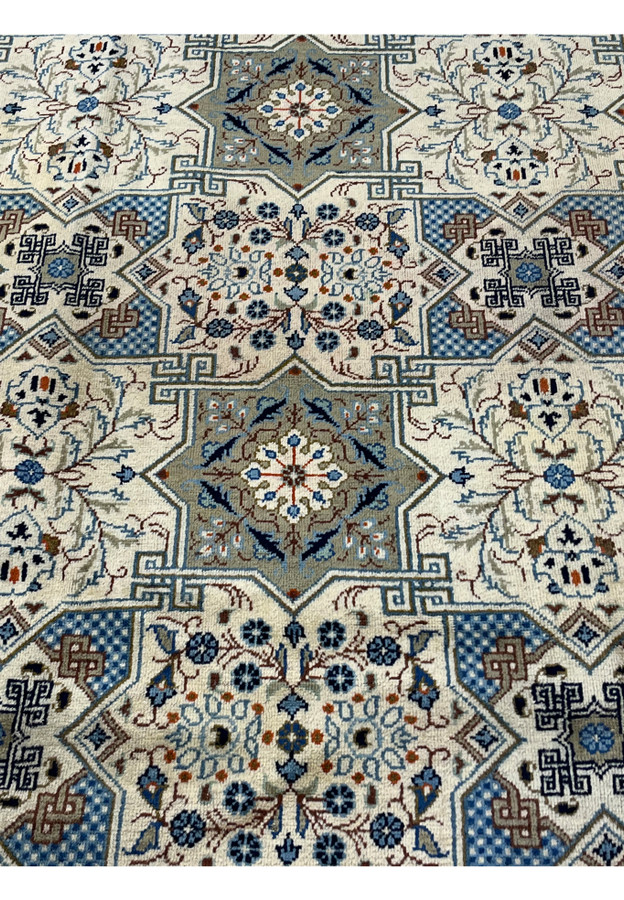 Macro detail of the Kheshti panel pattern on a Tabriz rug, highlighting a central star medallion with a symmetrical floral spray, surrounded by blue checkerboard diamonds and smaller rosette-filled compartments in navy and sage.