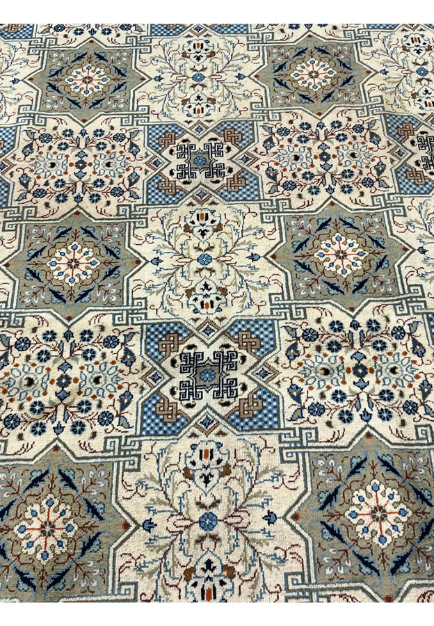 Low-angle perspective of a large Persian Tabriz carpet showing the full breadth of the rug with its repeating Kheshti compartment design, layered borders with diamond and floral motifs, and short fringed ends.