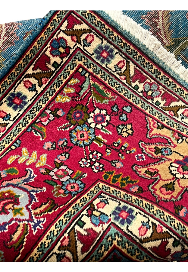 Folded corner of 10x13 Persian Tabriz rug showing crimson border against sky blue field