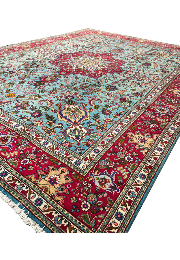 Angled view of 10x13 Persian Tabriz rug showing sky blue field and crimson medallion with red border