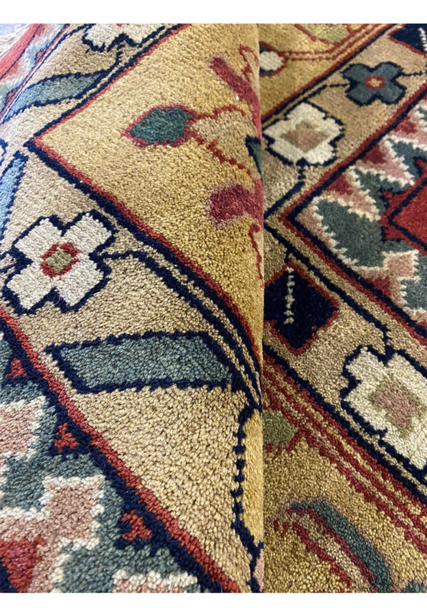 Rolled red and gold Oriental Agra rug showing thick wool pile and luminous Mughal floral design