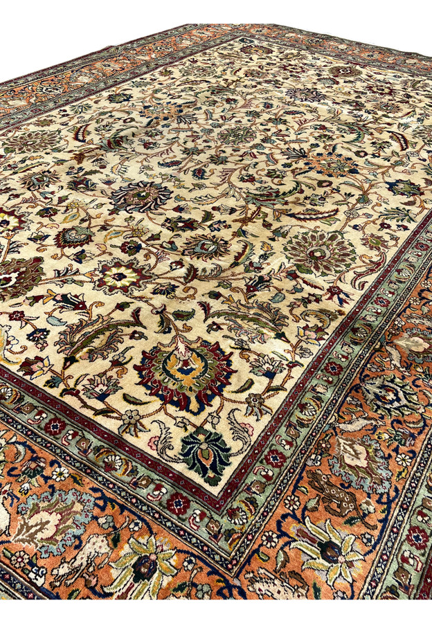 Angled three-quarter view of the cream and terracotta antique Tabriz showing the full allover floral composition in soft daylight