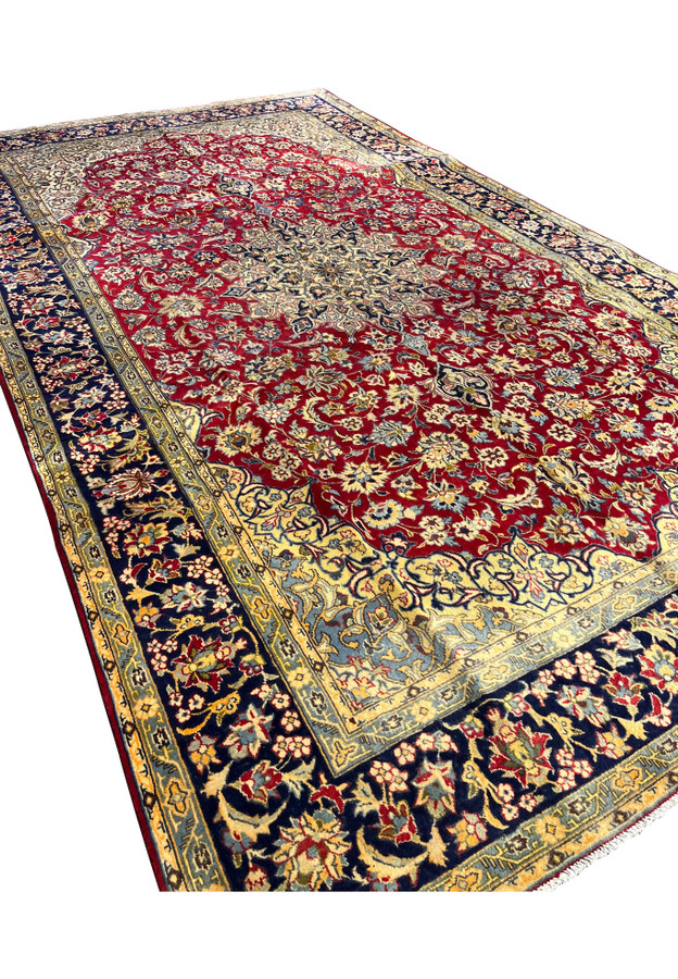 Angled three-quarter view of the deep red Isfahan revealing scale and the precise curvilinear drawing across the field