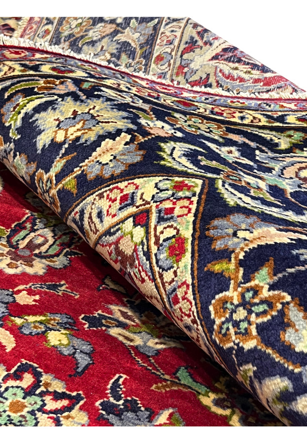 Persian Isfahan rug shown rolled at the edge revealing pile depth, navy main border, and bound selvage on hand-knotted wool