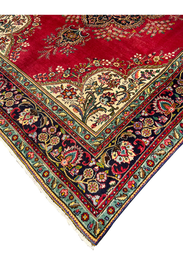 Corner detail of Persian Kerman rug showing ivory spandrel with rose floral bouquet meeting navy main border and turquoise guard stripe