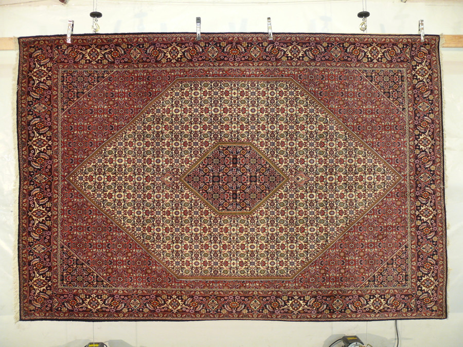 Persian Bijar rug shown hanging on display wall, full composition visible with ivory diamond and navy border framing