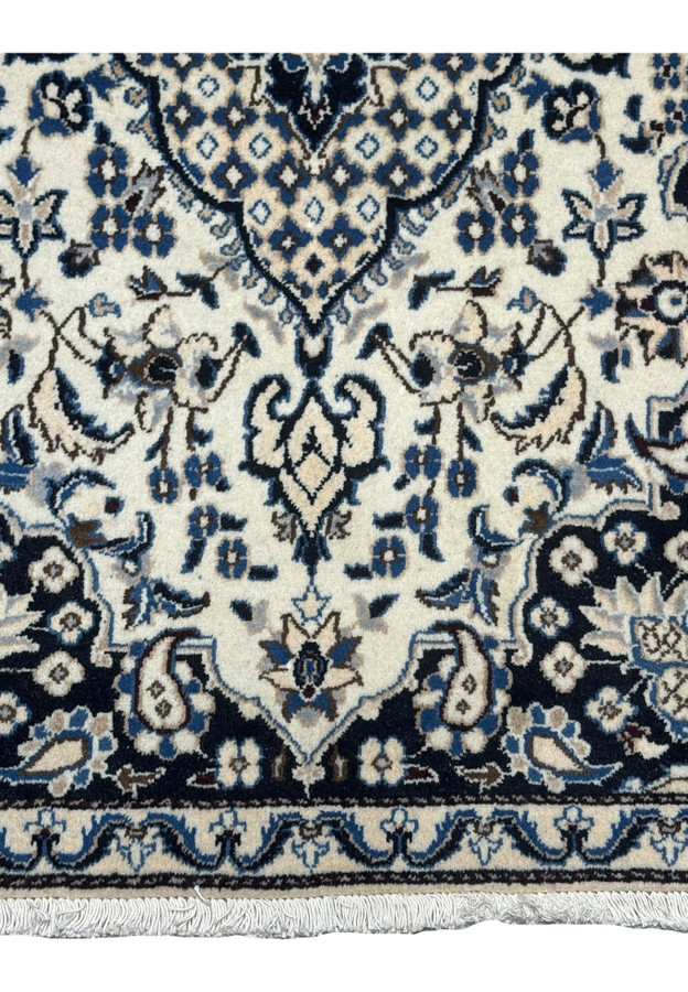 Lower field detail of Persian Nain rug showing palmette pendant, curling vines, and navy spandrel meeting ivory minor border