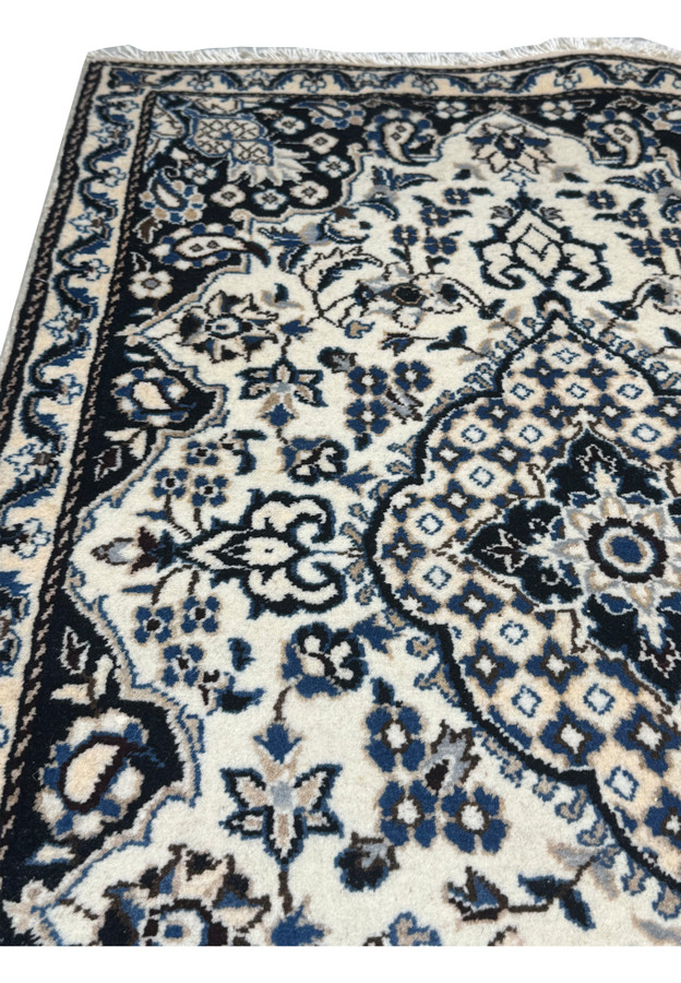 Upper corner detail of authentic Persian Nain rug, ivory minor border with rosette vine framing the navy floral main border