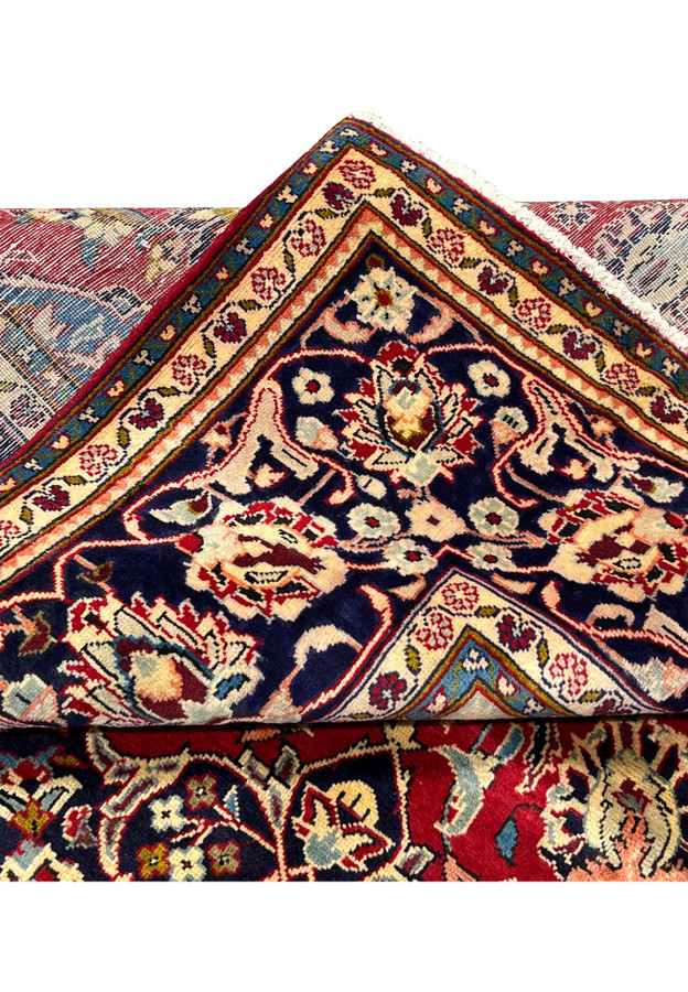Folded corner of 8x13 Persian Najafabad rug, navy border and ivory vine guard meeting rose red field along the crease