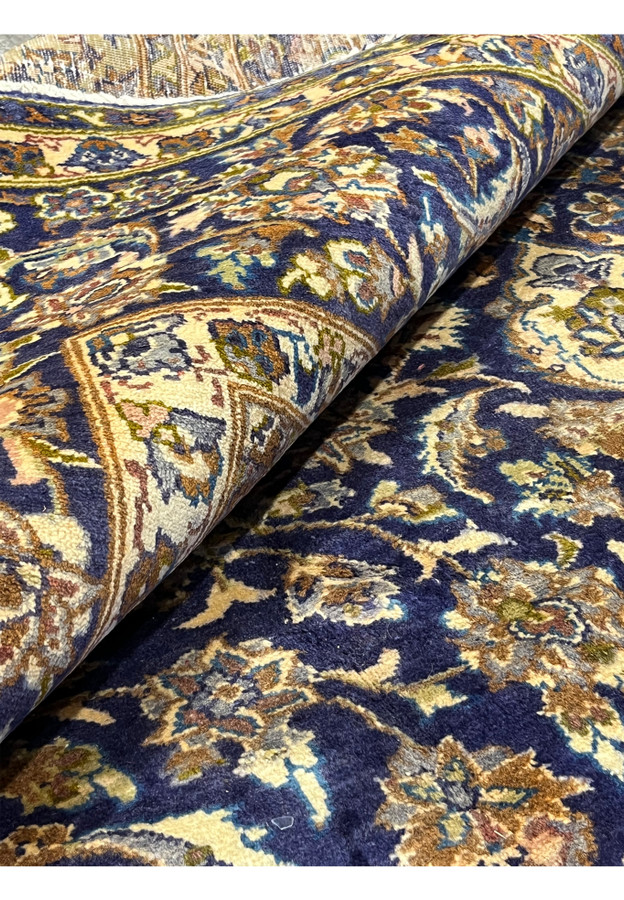Rolled corner of 10x13 Persian Kashan rug, dense wool pile, navy floral border framing navy field, hand-knotted
