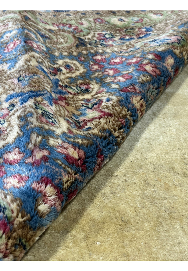 Rolled corner of oversize Persian Kerman rug, pastel floral border meeting ivory field, hand-knotted wool on cotton