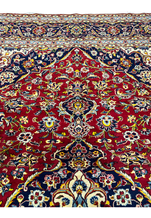 Upper field detail Persian Kashan rug, dense floral arabesque around navy spandrel on red field, classic medallion-and-corner layout