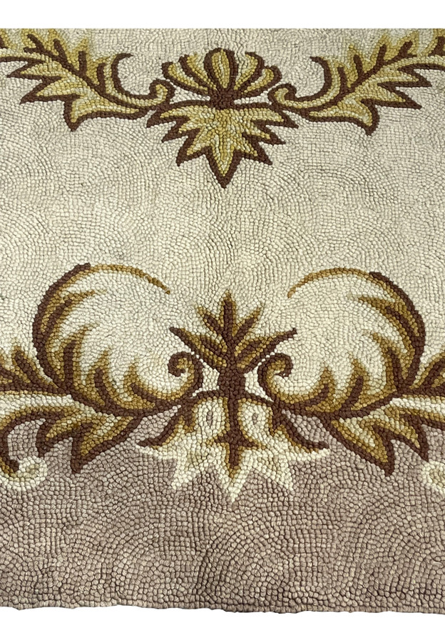 Brown and gold acanthus shell cartouche detail on the cream field of a vintage hand-hooked rug