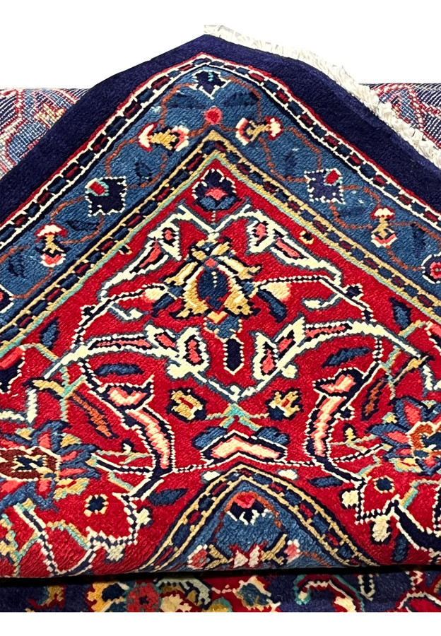 Folded corner of navy Mahal rug revealing red border, ivory fringe, and tight wool knotting