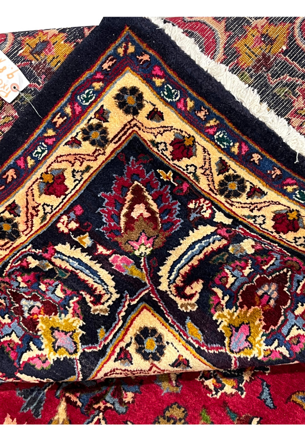 Back corner of the hand-knotted Mashad folded over showing the fine weave and binding