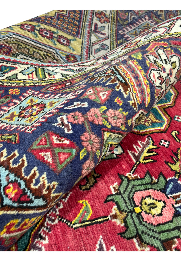 Rolled corner of the Tabriz revealing dense hand-knotted wool pile and vivid red and gold colors