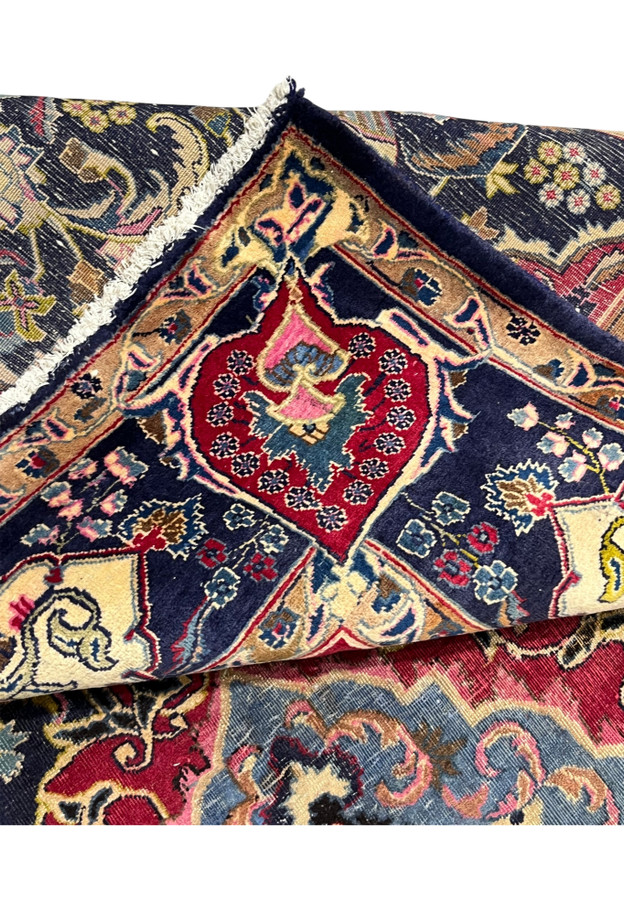 Folded corner of the Zirkhaki rug showing the hand-knotted back and red cartouche border