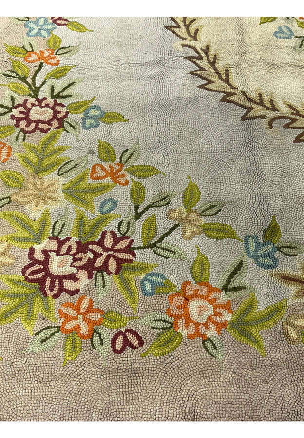 Orange and burgundy flowers with green leaves hooked in soft wool against a pale celadon ground