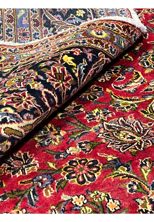 Vintage Kashan rolled to show the dense pile and red, navy, and ivory color blend.