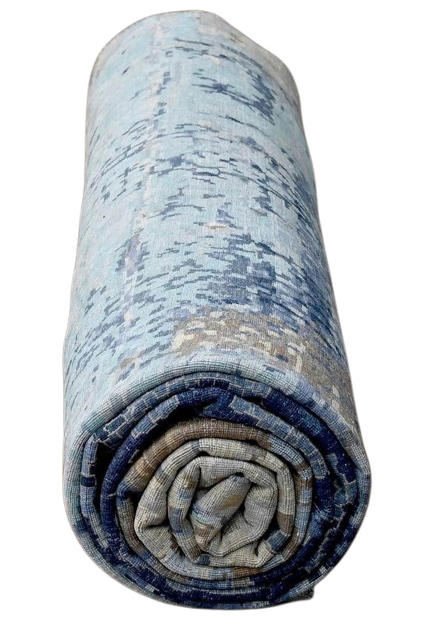 Rolled oversize blue abstract rug showing pale turquoise end and layered color transitions from light aqua to deep navy blue