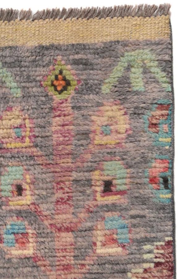 Close-up of grey Gabbeh rug end showing golden flatwoven finish and tribal motifs in pink, green and teal